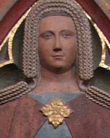 A large gold brooch fastening a lightweight mantle on the wife of a man in Bartholemeus Cathedral.